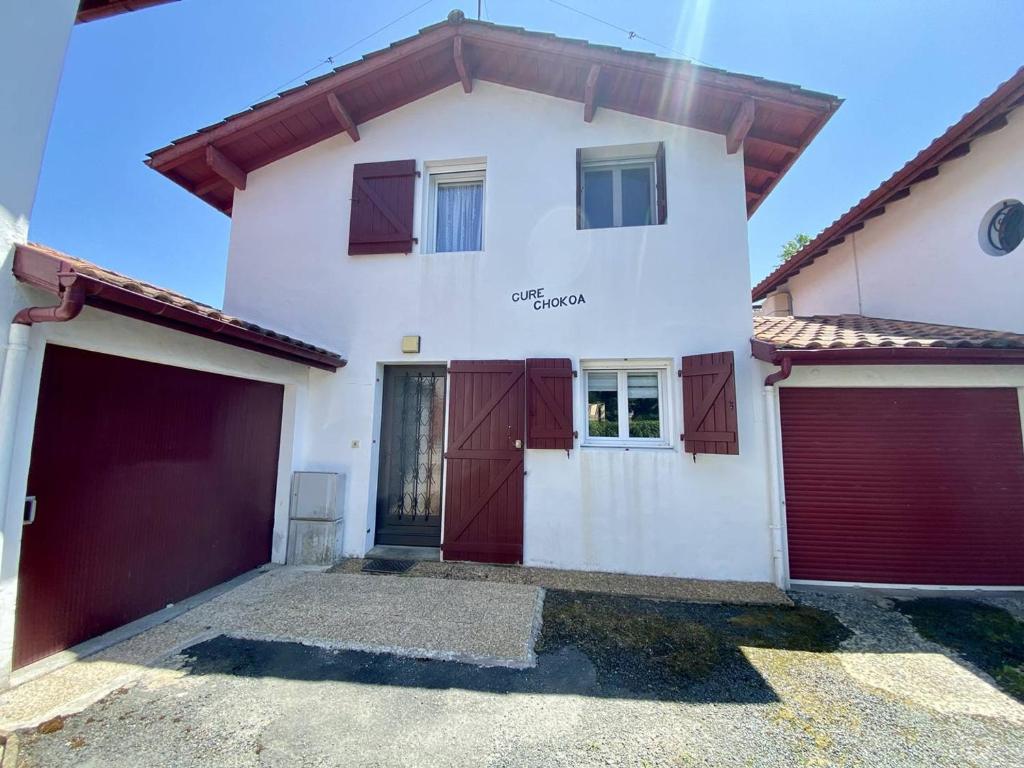 a large white house with red garage doors at Maison mitoyenne charmante, 3 pièces, 4 pers., parking, wifi, près centre-ville - FR-1-495-152 in Cambo-les-Bains