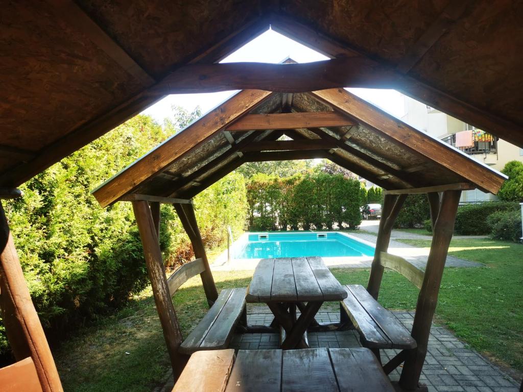 a picnic table and bench in a gazebo with a pool at Noémi Wellness Apartman in Siófok