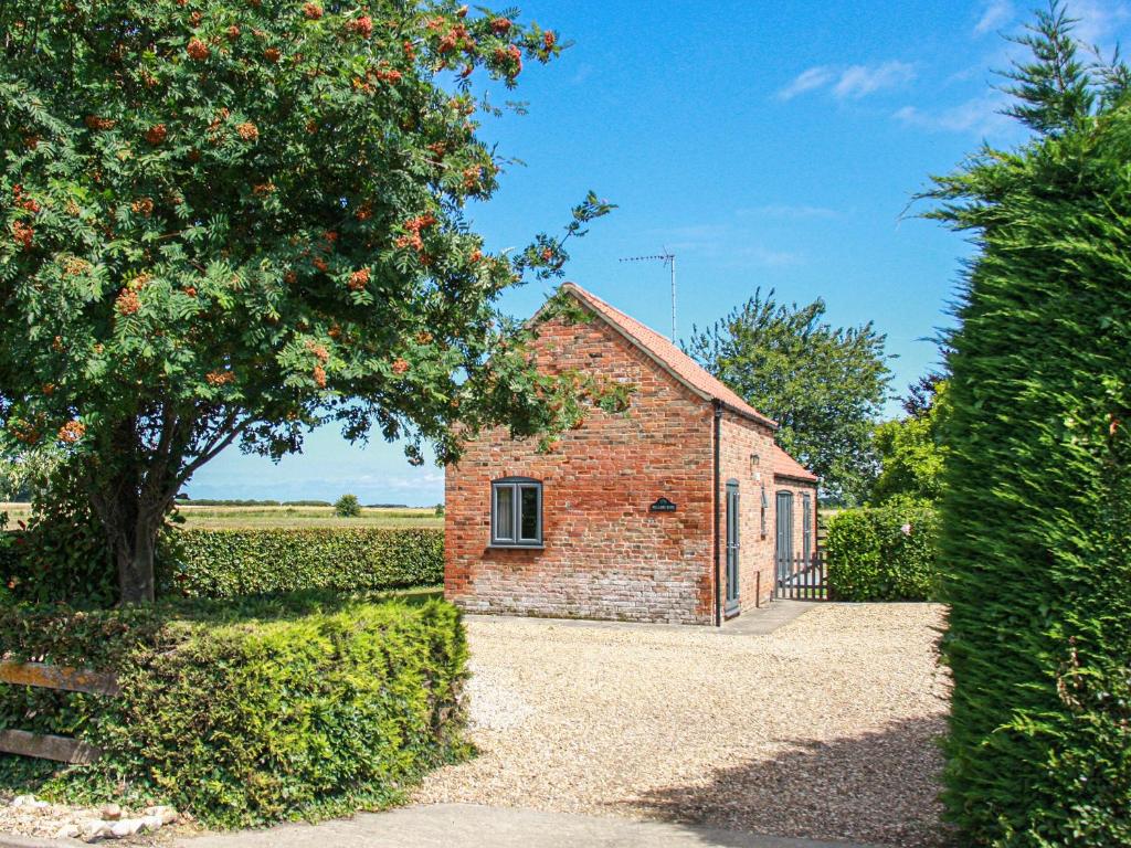 a brick building with a tree and a fence at Willows Barn in Clenchwarton