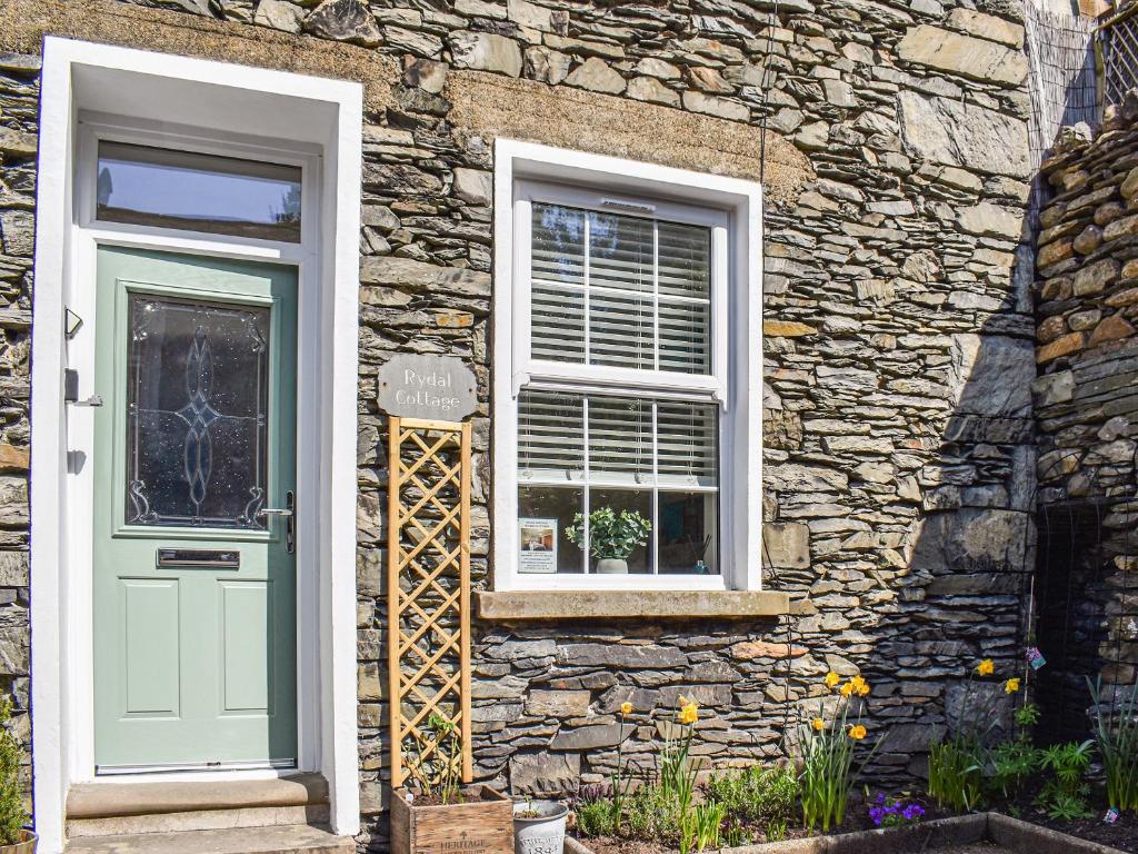a stone house with a green door and a window at Rydal Cottage in Bowness-on-Windermere