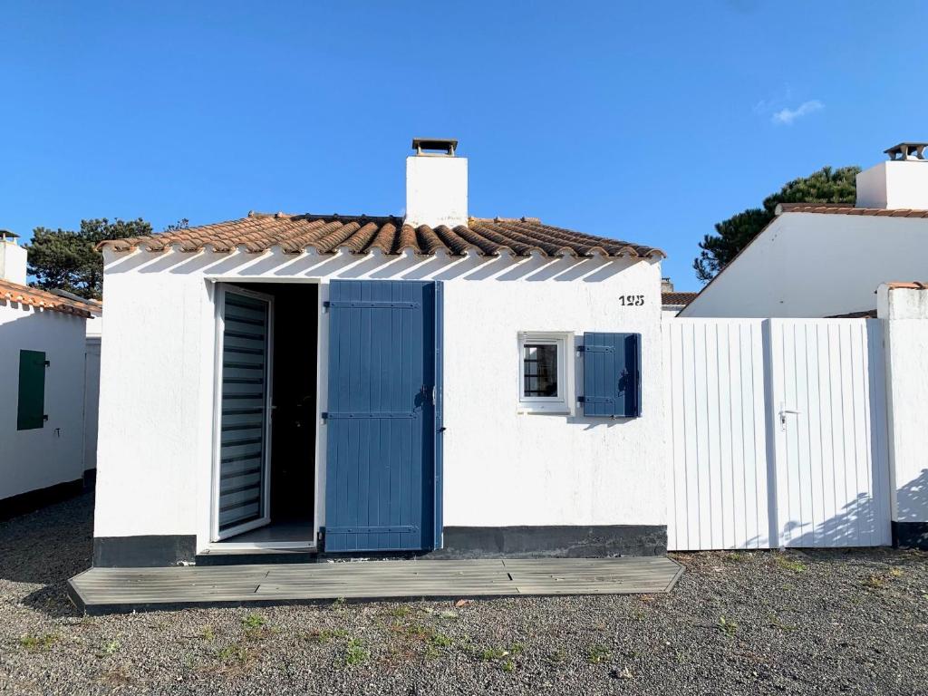 une petite maison blanche avec une porte bleue dans l'établissement Charmante maison T2 avec piscine chauffée, tennis, proche mer, commerces, et WiFi inclus - FR-1-231-307, à Bretignolles-sur-Mer
