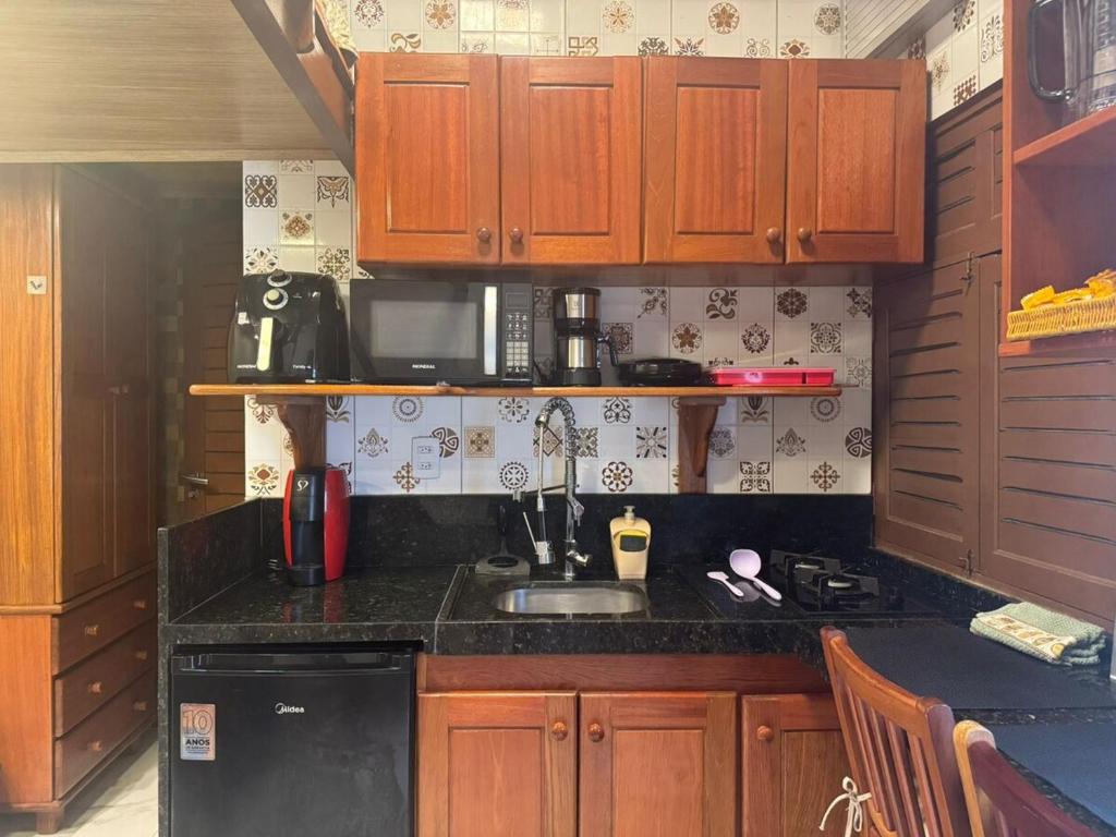 een keuken met houten kasten en een zwart aanrechtblad bij 05 Kitnet próximo da praia com ar-condicionado in Maceió