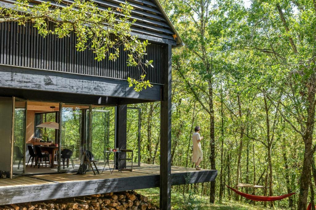 une maison dans les bois avec une femme debout sur une terrasse dans l'établissement Designer House In The Vézère Forest, à Valojoulx