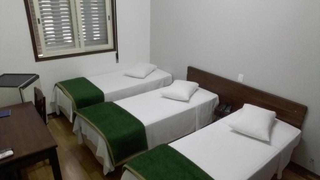 um quarto com duas camas e uma mesa e uma janela em Arcadas Hotel em Caçapava