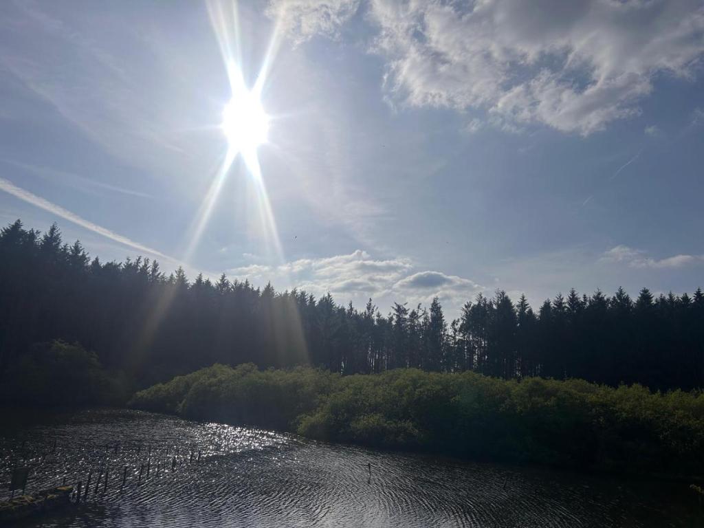 a sun is shining over a river with trees at Bell Tent - Lakeside in Oswestry