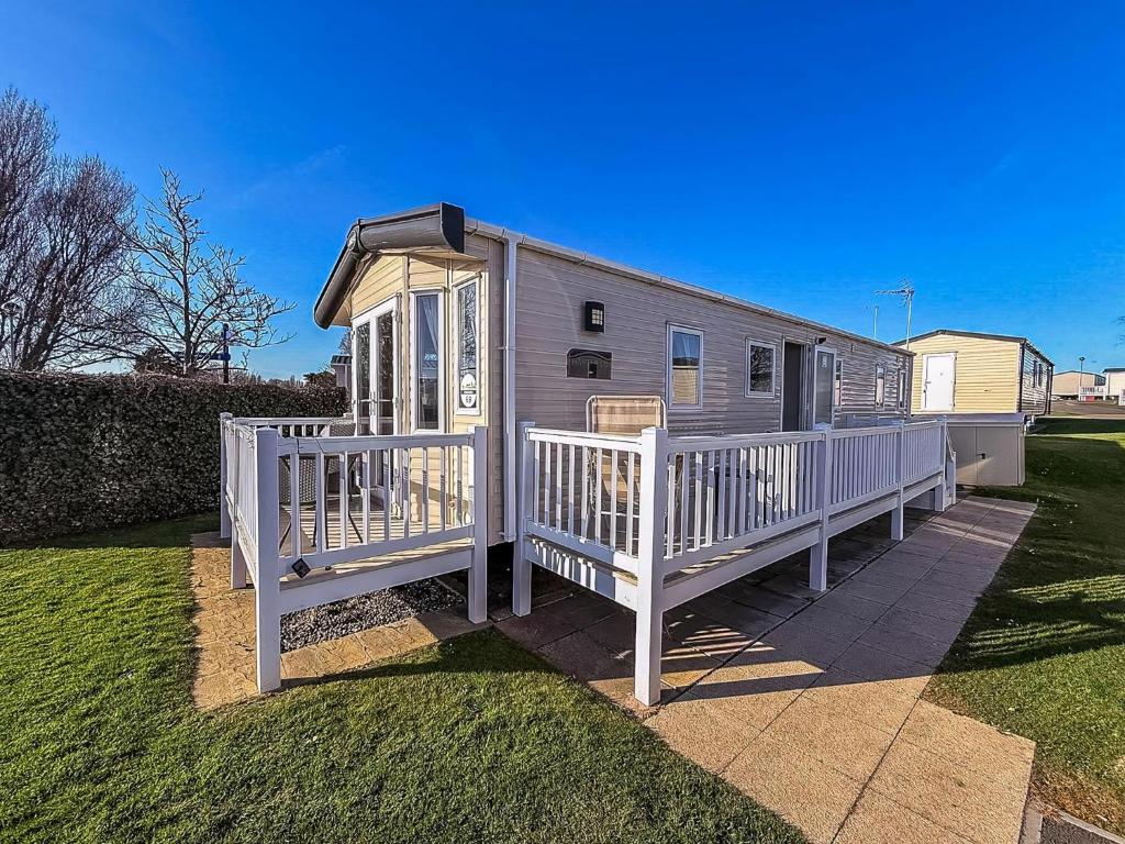 a tiny house with a white fence in a yard at Fantastic Caravan With Decking At Haven Hopton Holiday Park Ref 80069G in Great Yarmouth
