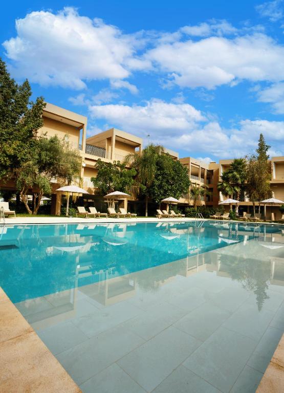 a large swimming pool with chairs and umbrellas at Rawabi Hotel Marrakech & Spa in Marrakesh