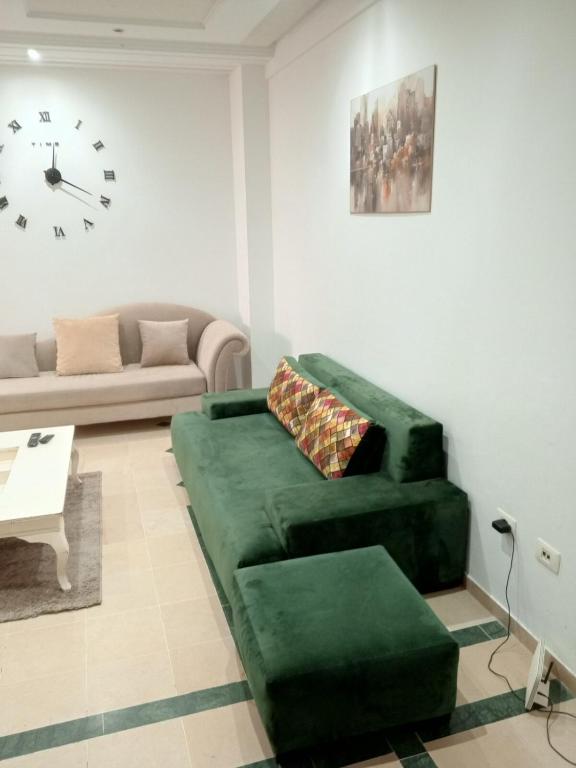 a living room with a green couch and a clock at Le bon sejour in El Aouina Station