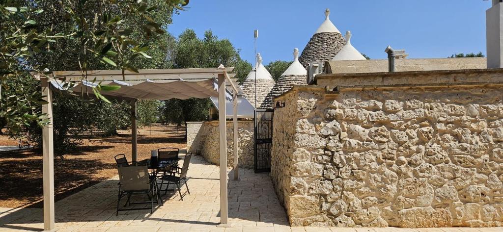 un mur en pierre avec une table, des chaises et un parasol dans l'établissement Trullo Le Rondinelle, à San Michele Salentino