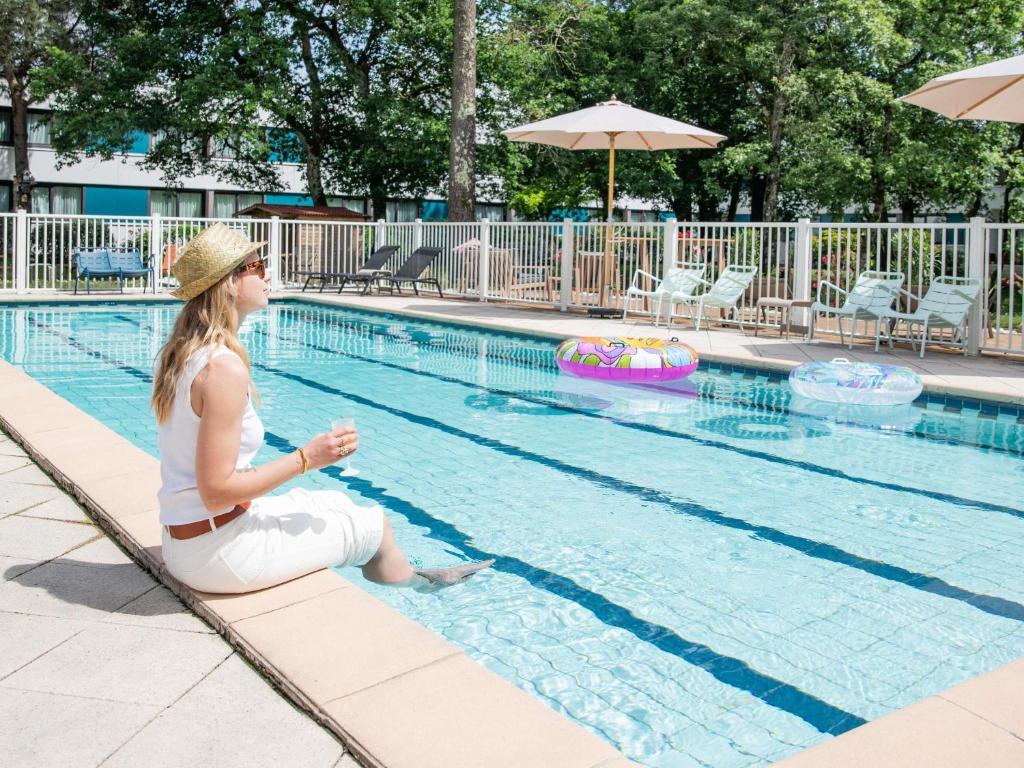 une femme assise au bord d'une piscine dans l'établissement Novotel Bordeaux Mérignac, à Mérignac