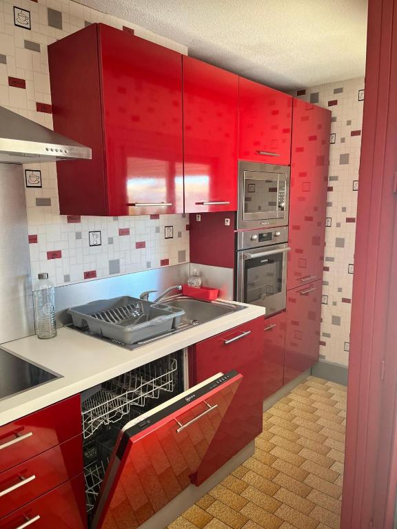 - une cuisine rouge avec des placards rouges et un évier dans l'établissement Le Volvire 31, au Cap d'Agde