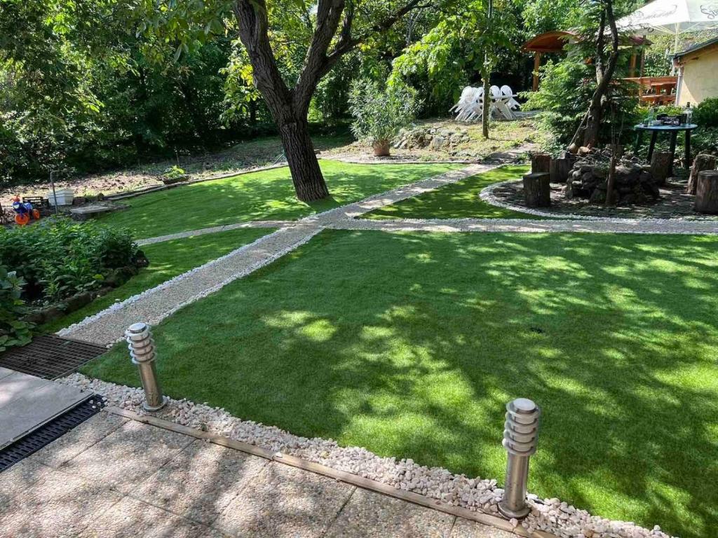 un patio verde con un árbol y una acera en Gergely Apartman, en Pálosvörösmart
