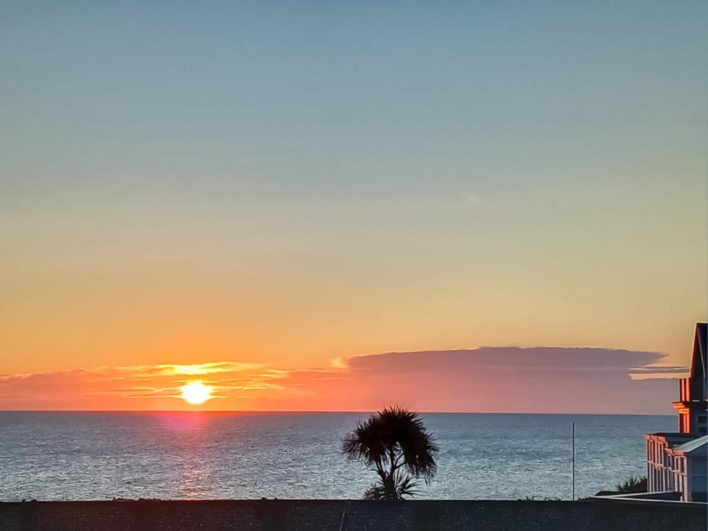 una puesta de sol sobre el océano con una palmera en Zero Degrees North, en Sheringham