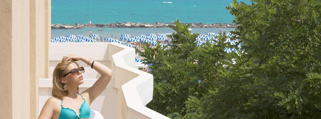 a woman standing next to a building with a view of the beach at Hotel Cristina Corona in Cattolica