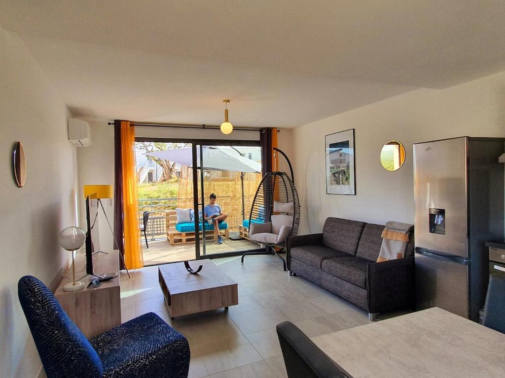 un salon avec un canapé et une personne assise sur une balançoire dans l'établissement T2 Yucca LCP - Beautiful 48 m2 2-room, 17 m2 terrace, new, air conditioning, à Grosseto-Prugna