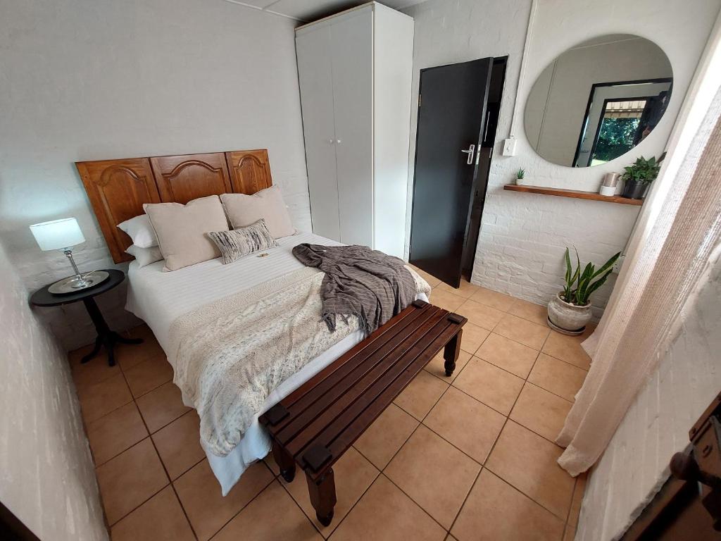 Dormitorio con cama con banco y espejo en Hill Top Cottage, en Pietermaritzburg