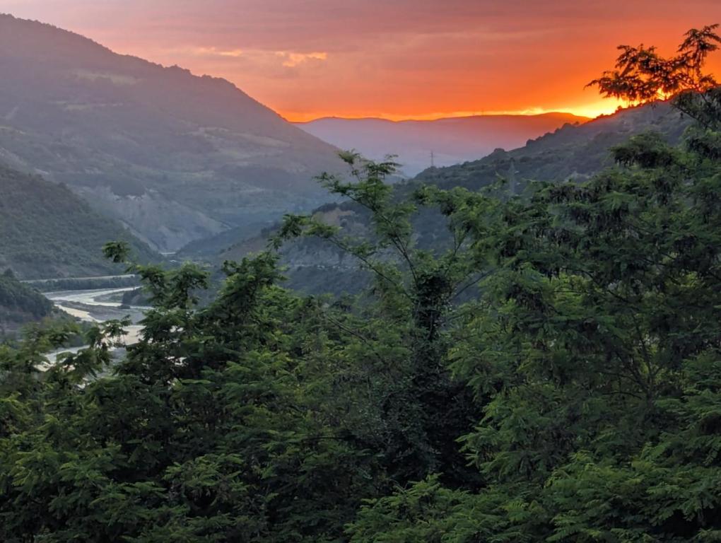 a sunset in the mountains with trees and a river at Rina's Appartment in Çorovodë