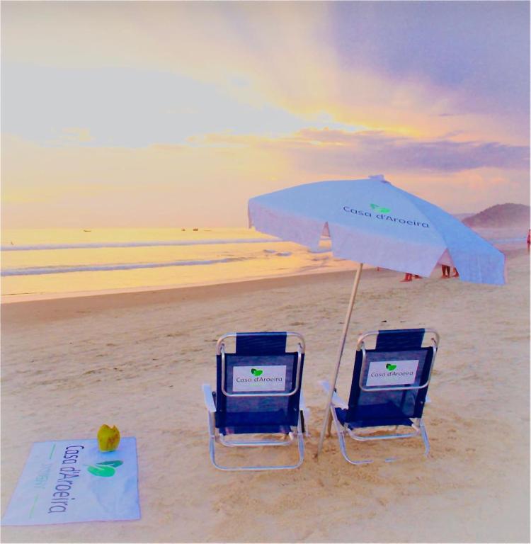 朱奎Casa d'Aroeira Residencial Boutique - Centro de Juqueí - 2 quadras do mar - Serviço de Praia - Roupa de Cama 600 fios algodão Egípcio - Toalhas Banho e Praia - Tudo Novo - Estacionamento Interno - Cozinha - Consulte unidades com Ofurô Hidro e Cromoterapia的海滩上的两把椅子和一把遮阳伞