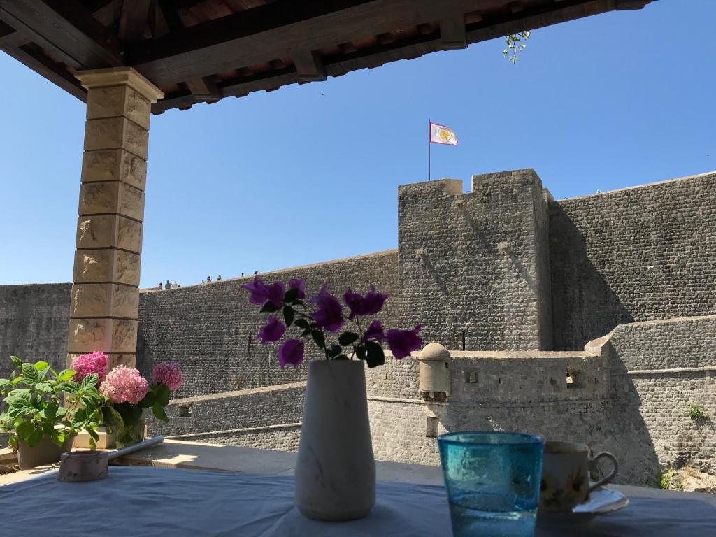 a vase with purple flowers on a table with a castle at Apartment STONE by City Walls in Dubrovnik