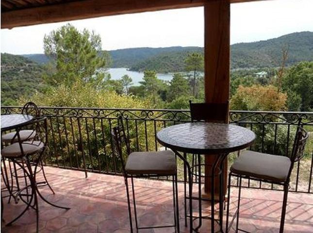 a balcony with tables and chairs and a view of the water at Les Gîtes du Lac in Montauroux