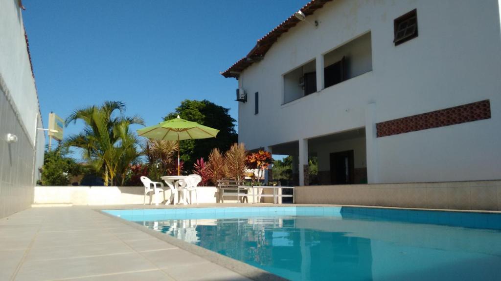 a house and a swimming pool with a table and an umbrella at Kazaya Pousada in Araruama