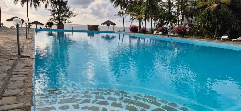 a large blue swimming pool with palm trees and the ocean at Zuri Twin Sands Beach Properties - Malindi in Malindi