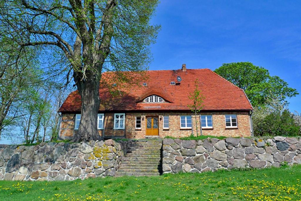 a brick house with a red roof and a stone wall at Gutshaus Jülchendorf in Jülchendorf
