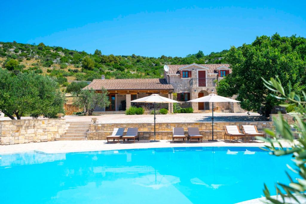 a pool with chairs and umbrellas in front of a house at Lavanda Mansion in Vodice