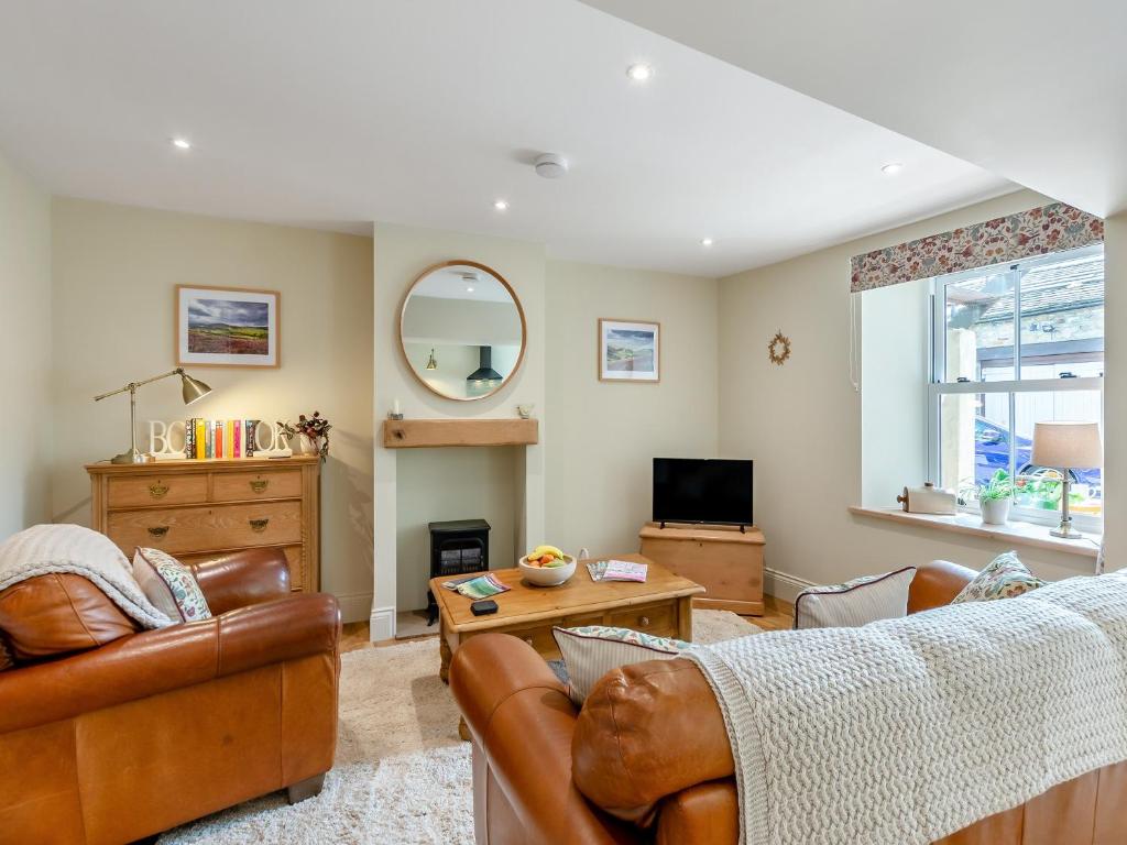 a living room with leather furniture and a tv at Courtyard Cottage in Reeth