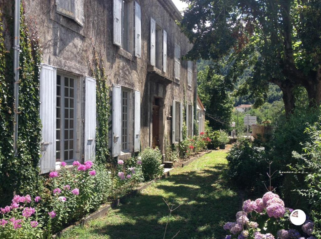 une vieille maison en pierre avec des fleurs dans la cour dans l'établissement Maison de famille Victorine, à Lamastre