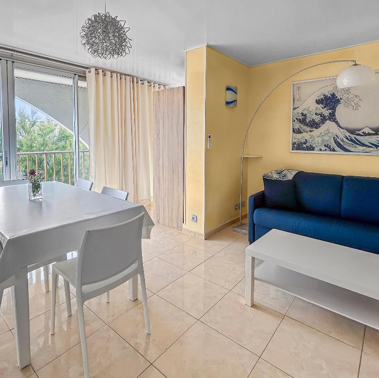 Una sala de estar con una mesa y un sofá azul. en T2, Calme & lumineux, au bout du jardin, la plage!, en La Grande-Motte