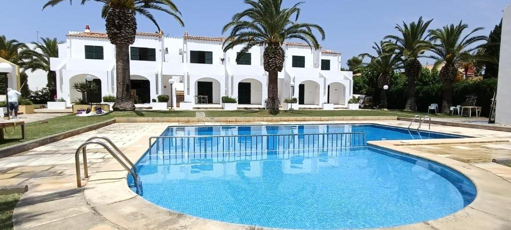 a pool in front of a white house with palm trees at Apartamento costa Menorca in Cala en Bosc