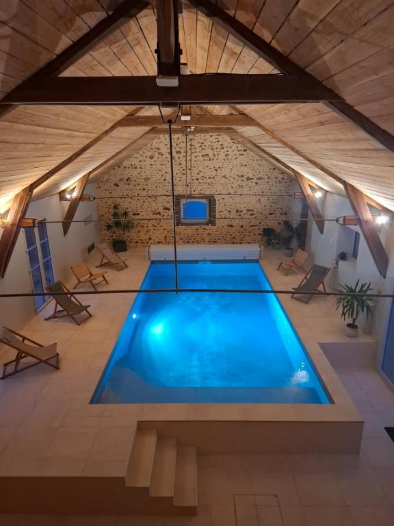 - une grande piscine dans un bâtiment doté d'un plafond en bois dans l'établissement La Grange Flor'Alie gîte et piscine intérieure, à Meslay-le-Grenet