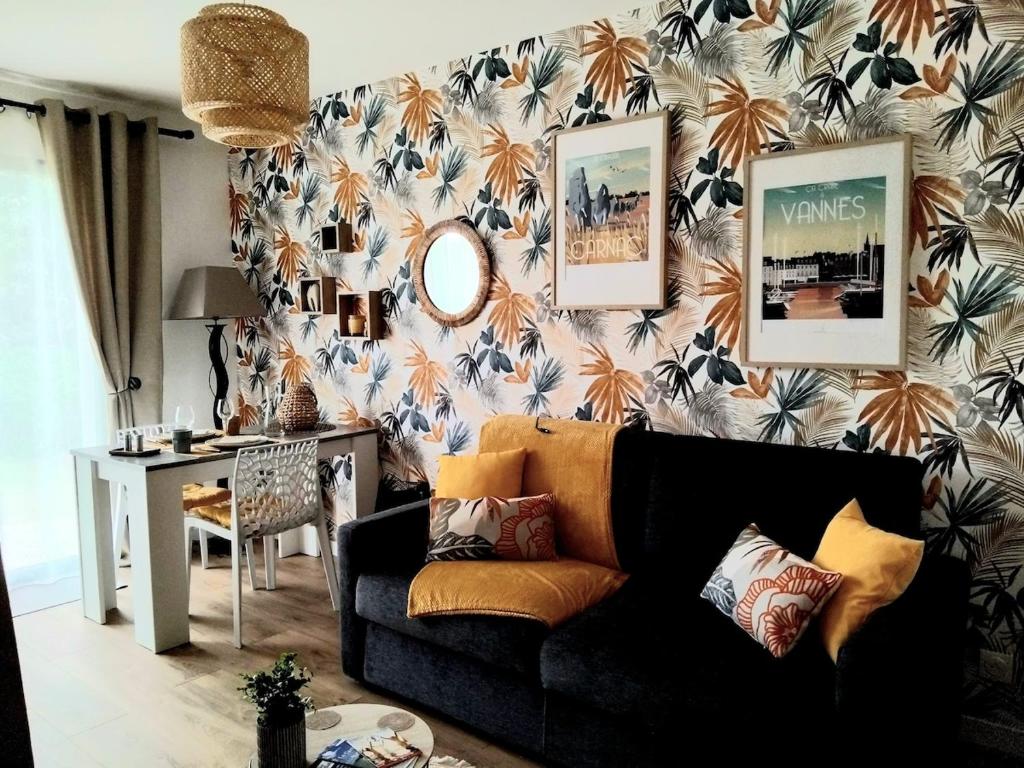 - un salon avec un canapé noir et du papier peint floral dans l'établissement Votre joli studio cosy à Meriadec, à Pluneret