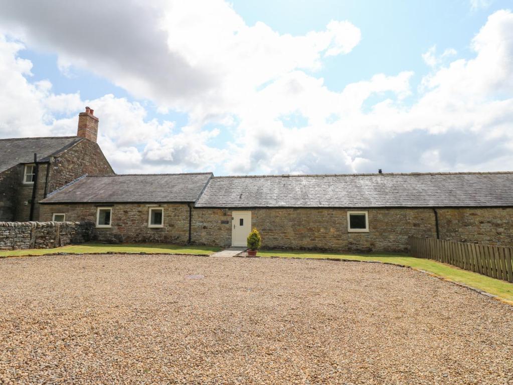 una antigua casa de piedra con una entrada de grava en Shepherds Burn Cottage, en Greenhaugh