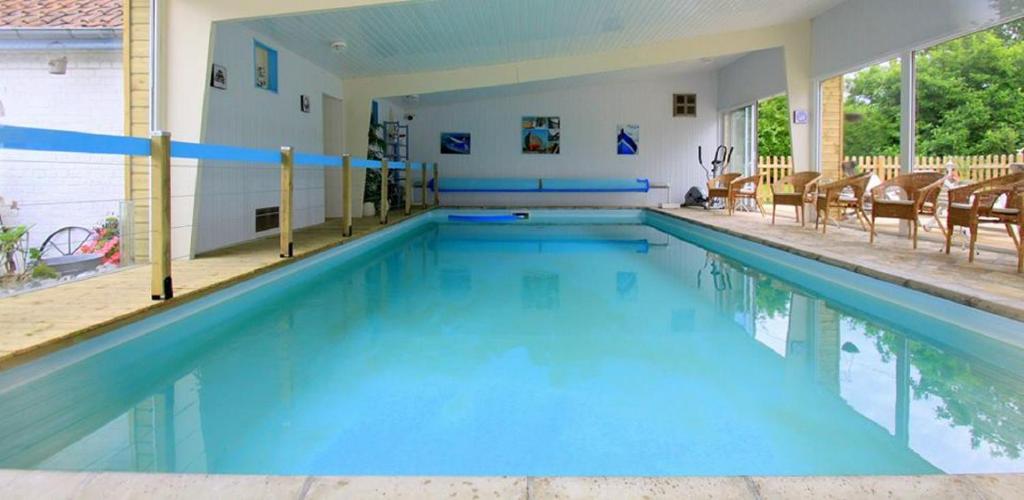 a large swimming pool with blue water and chairs at Les Songes de l'Authie in Boufflers