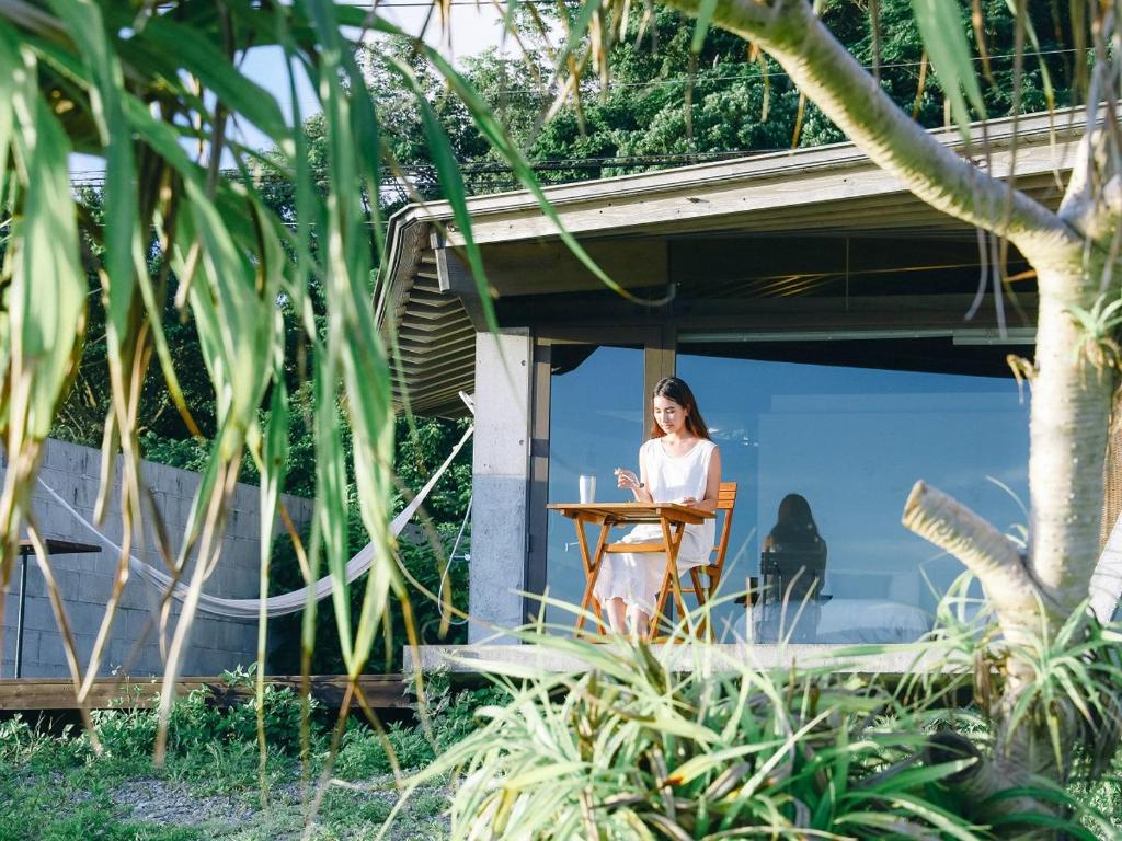 a woman sitting at a desk in front of a house at Denpaku The Beachfront MIJORA in Amami
