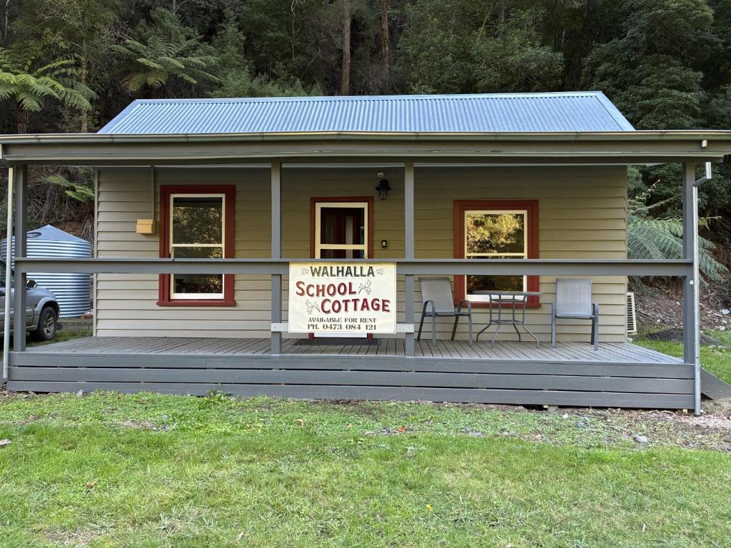 une petite maison jaune avec un panneau sur un porche dans l'établissement School Cottage, à Walhalla