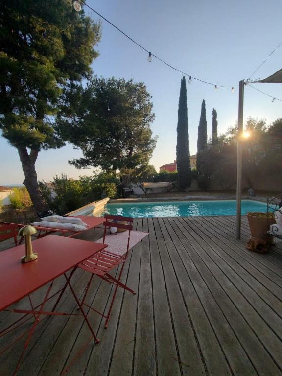 une piscine avec une table et des chaises rouges sur une terrasse en bois dans l'établissement Villa neuve avec piscine et vue panoramique, à La Fare-les-Oliviers
