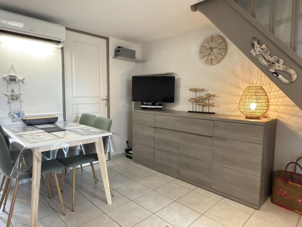 un salon avec une table avec des chaises et une télévision dans l'établissement Petite maison avec jardin & piscine partagee, à Valras-Plage