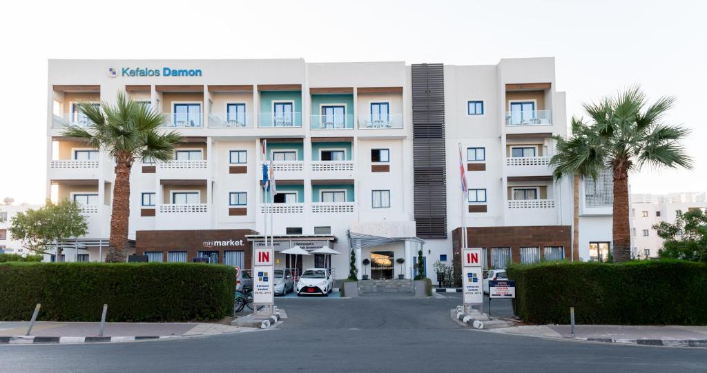 a large white building with palm trees in front of it at Kefalos Damon Hotel Apartments in Paphos