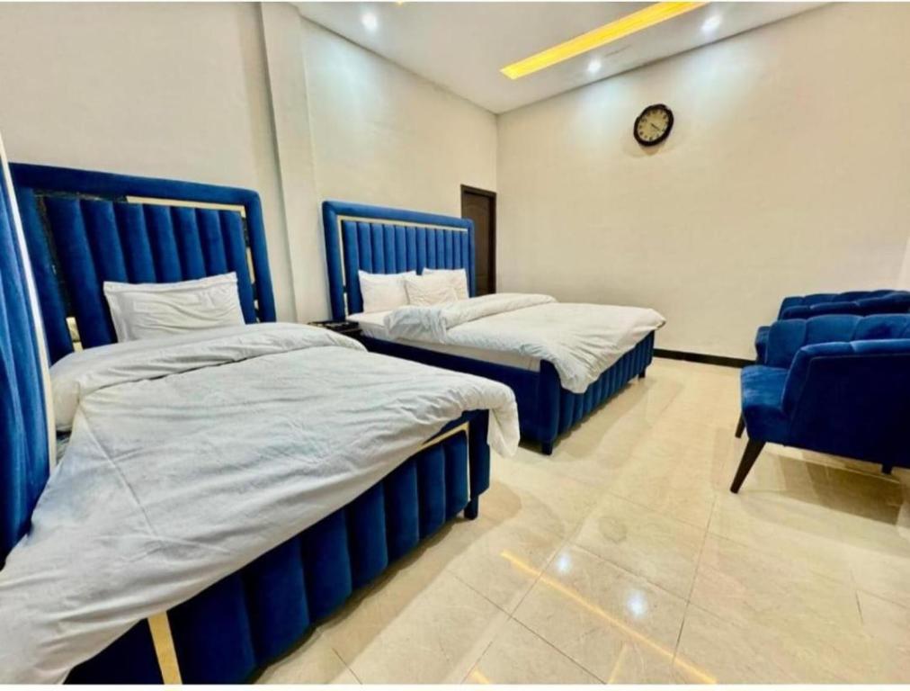 twee bedden in een kamer met een stoel en een klok bij Islamabad Comfort Inn in Islamabad