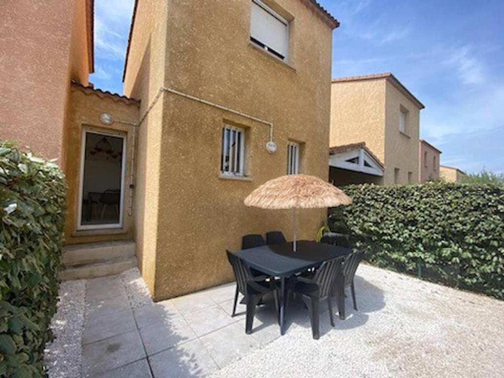 a table with chairs and an umbrella in front of a building at Valras-Loc Maison T3 in Valras-Plage