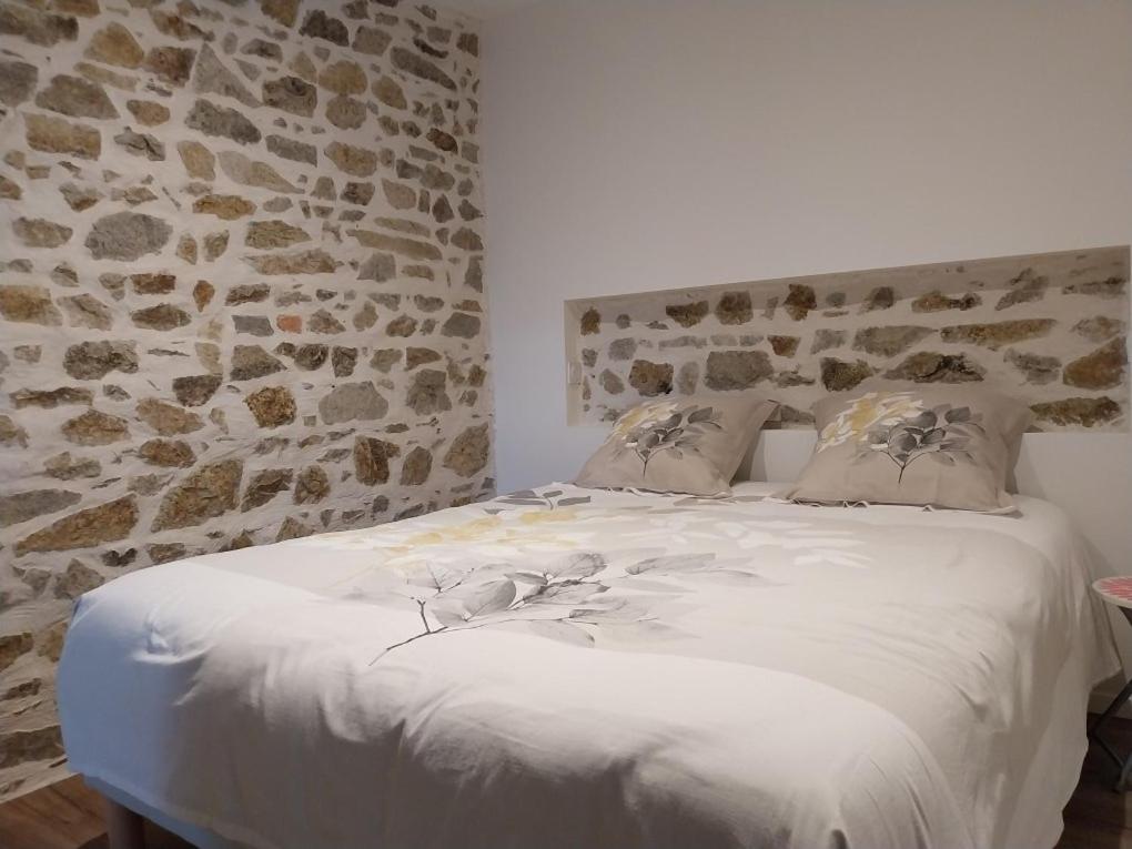 a bedroom with a white bed with a stone wall at La Petite Ferme Aux Prés in Saint-Germain-Lespinasse