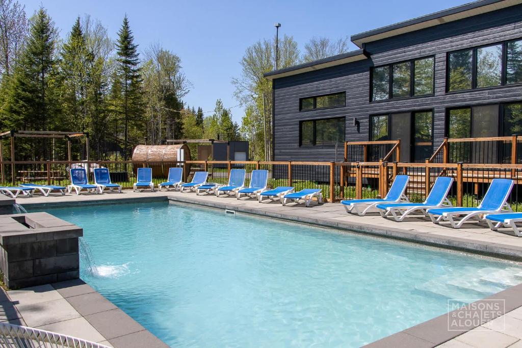 a swimming pool with lounge chairs and a house at Chalet Beaulieu - Spa - Piscine - Sauna - Billard in Pont-Rouge
