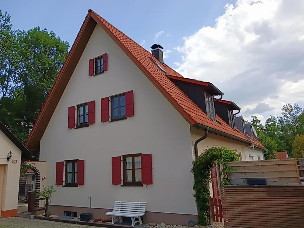 a white house with red windows and a bench at Ferienwohnung Dießen Bierdorf - Holzacker in Dießen am Ammersee