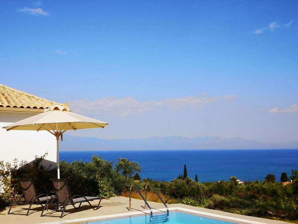 a swimming pool with an umbrella and chairs and the ocean at The Iconpainter Kalamaki Villa in Kómboi