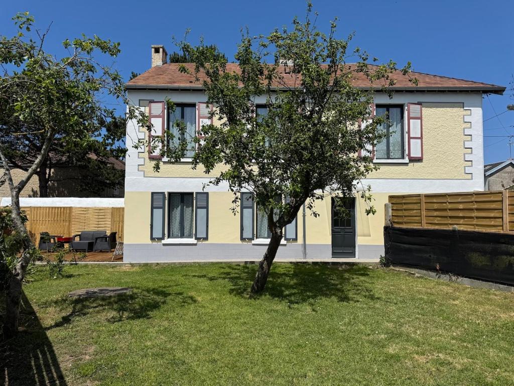 a large yellow house with a tree in the yard at Chez Sylviane Rez-de-Chaussée 200 m de la mer in Luc-sur-Mer