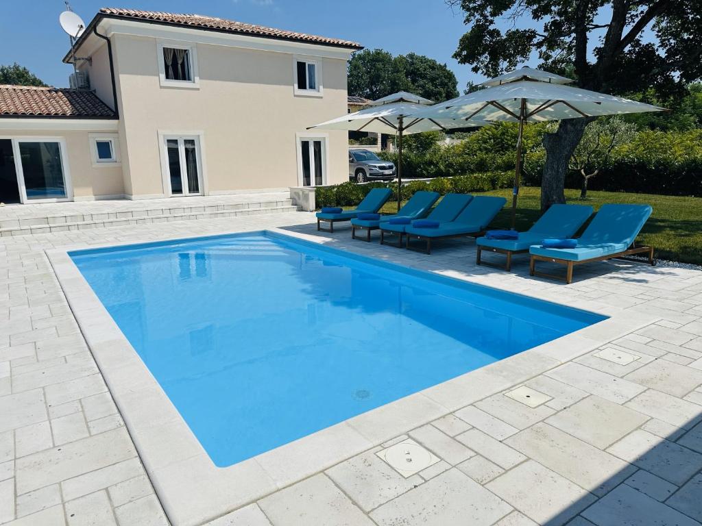 a swimming pool with blue chairs and an umbrella at Villa V in Svetvinčenat