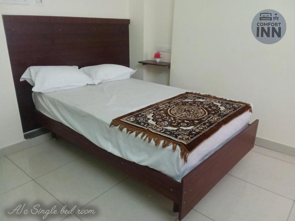 a bed with a wooden headboard and white pillows at Comfort inn Lodge Tirunelveli in Tirunelveli